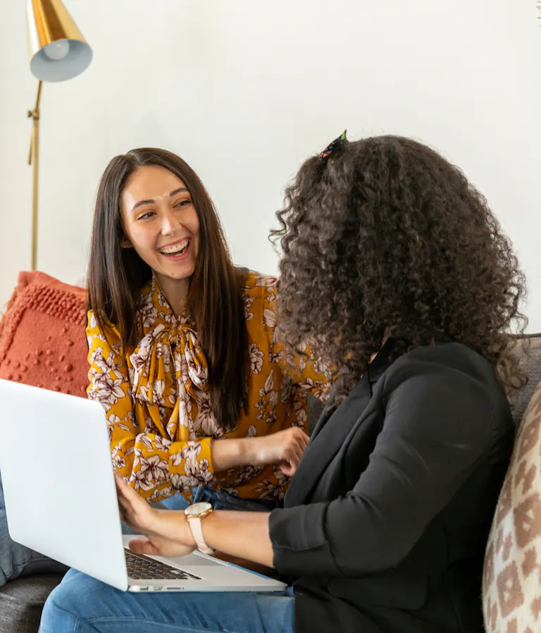 Two woman with laptop laughing on couch
