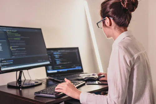 Woman coding on two computers