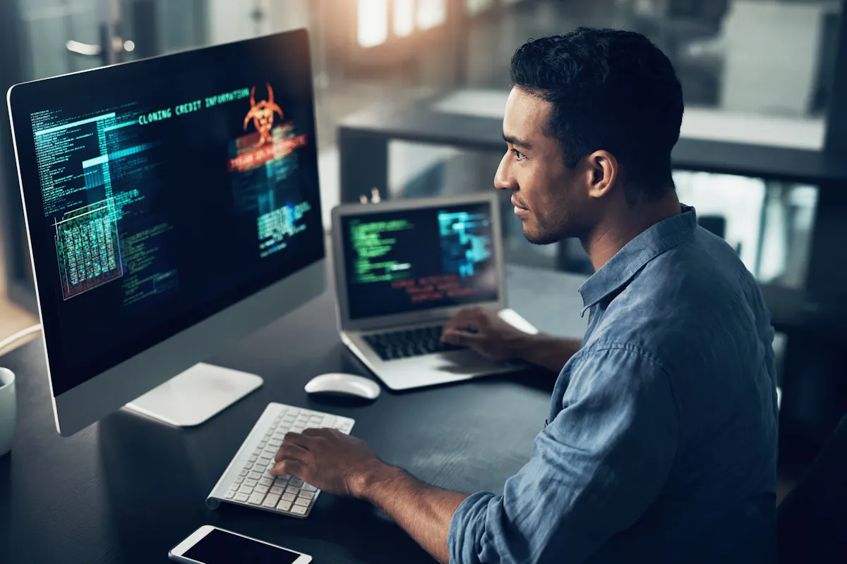 A cybersecurity professional works on a laptop and a desktop computer.