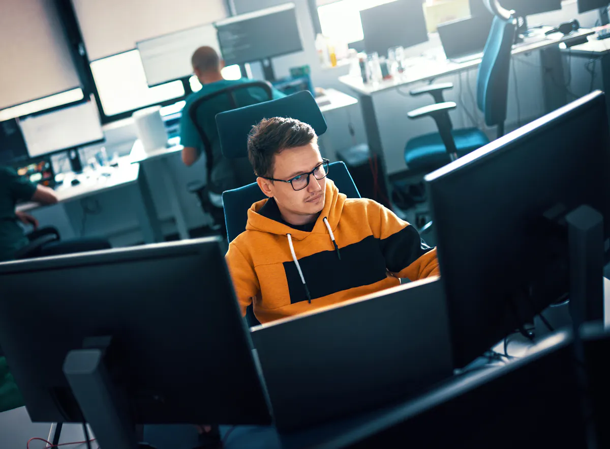Student focused in yellow sweatshirt coding at office