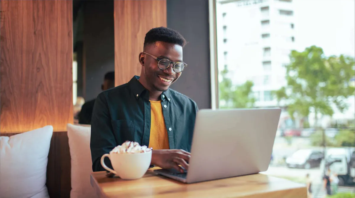 Man at coffee shop smiling on laptop