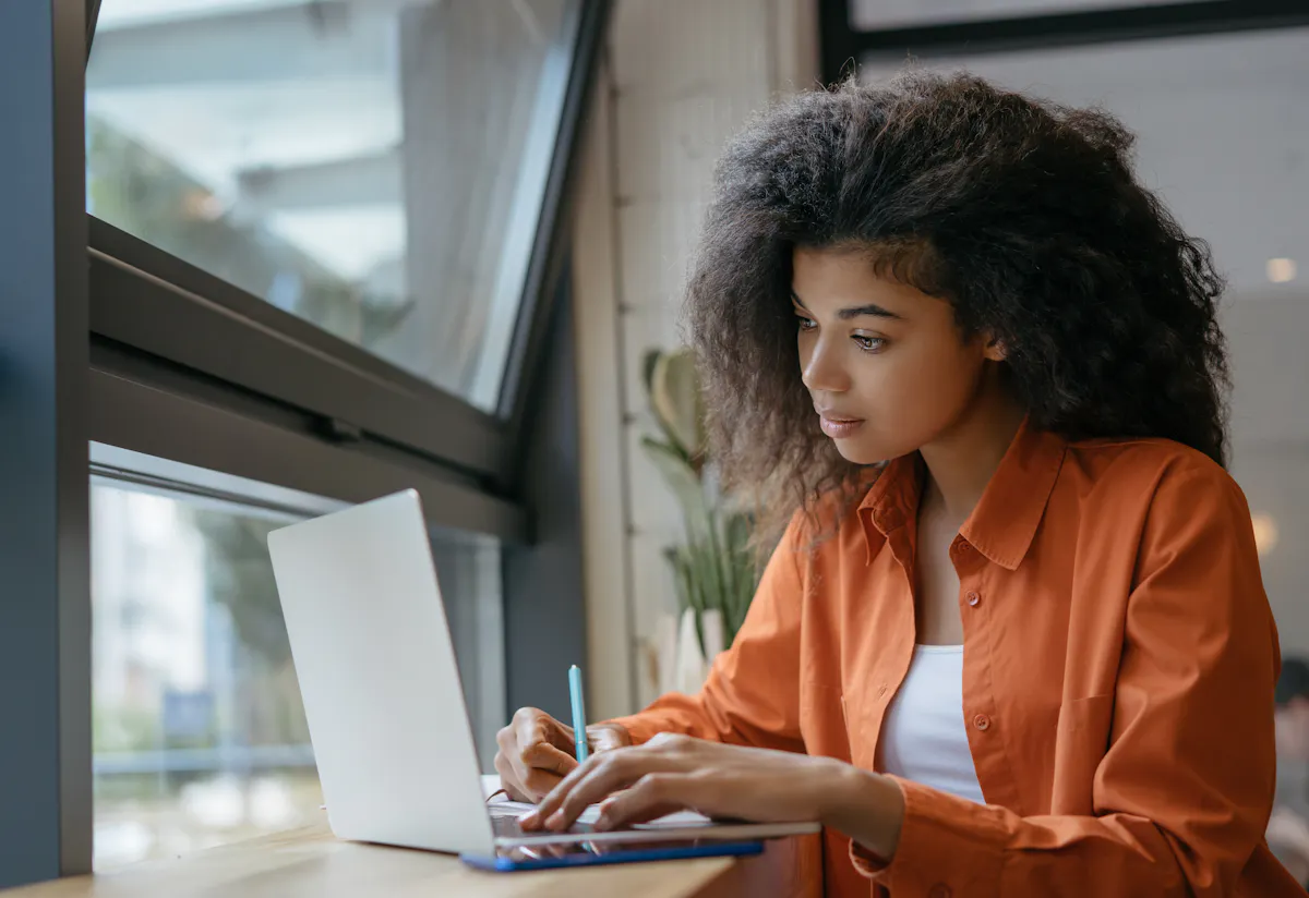Black woman working indoors on silver laptop
