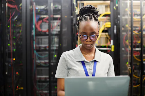 A cybersecurity professional works on a laptop in a server room.
