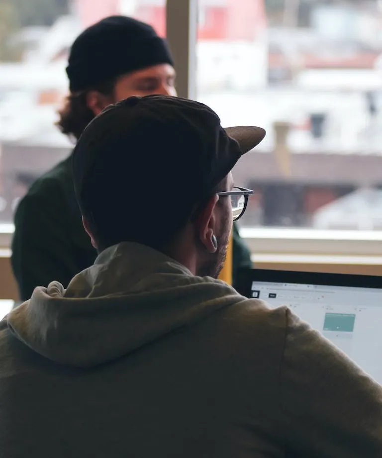 Man with glasses working on laptop with other man in background