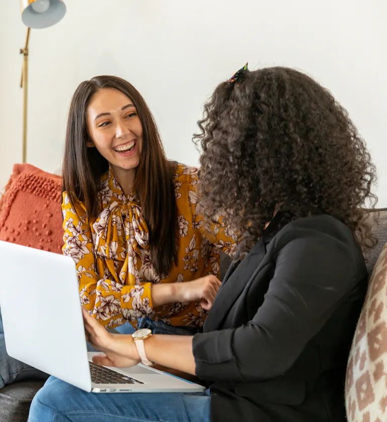 Two woman with laptop laughing on couch