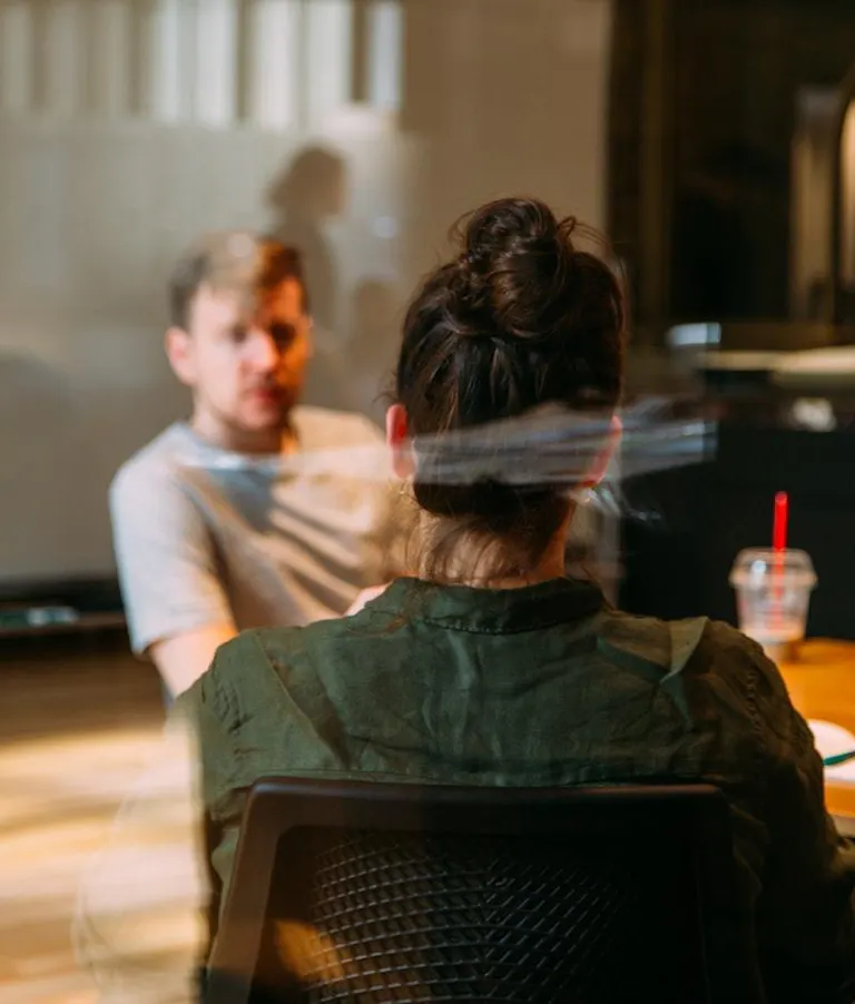 Woman talking to man behind glass conference room